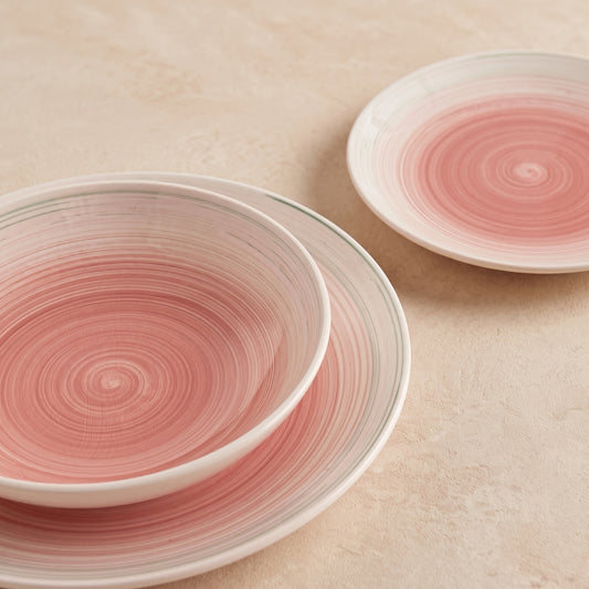 Velvet serviesset van drie roze handgeschilderde borden op een beige tafel, van dichtbij