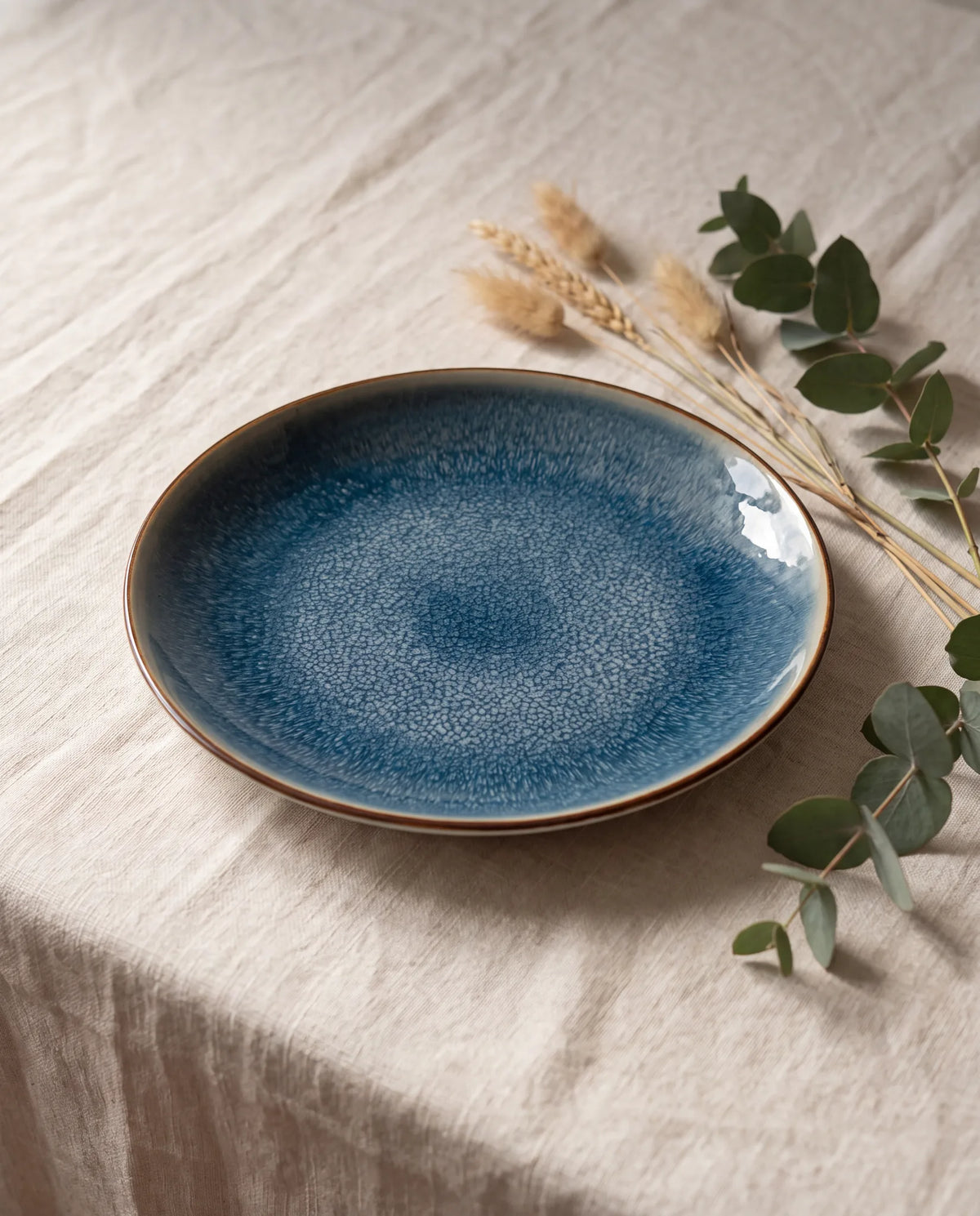 Aura bord – New Bone porselein met blauw reactief glazuur en fijne bruine rand, op linnen