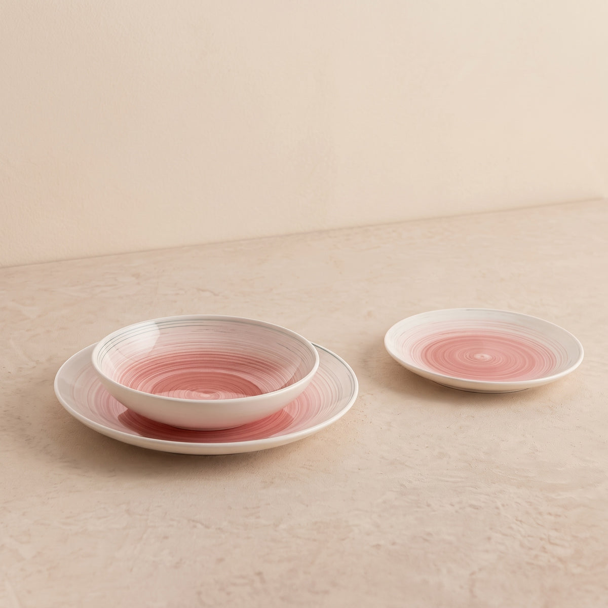 Velvet serviesset van drie roze handgeschilderde borden op een beige tafel, in zijaanzicht