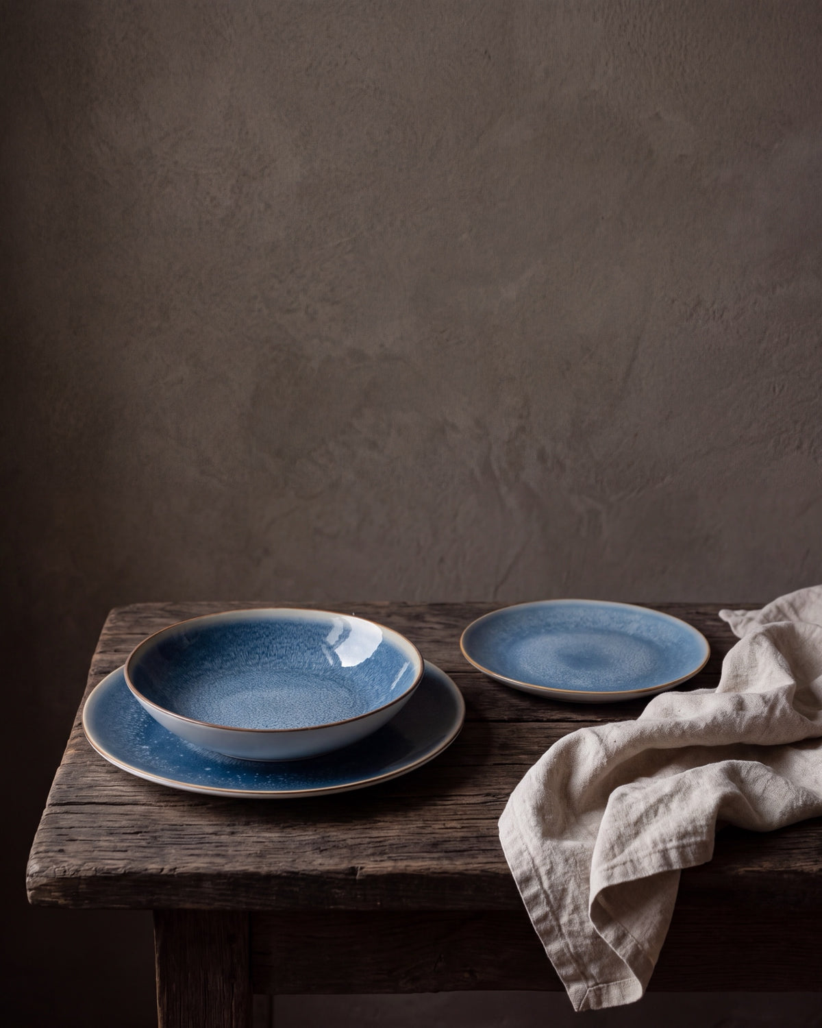 Aura servies op een houten tafel voor een lemen wand: dinerbord, diep bord en dessertbord