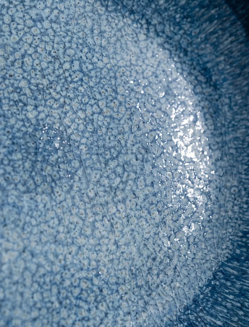 Gros plan sur l'émail bleu d'une assiette Aura avec un reflet de lumière