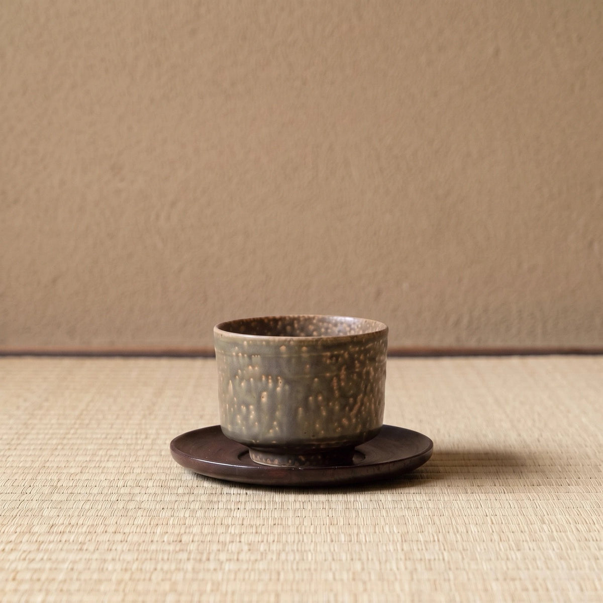 Cypress koffiekop op een houten onderzetter, op tatami voor een leemwand