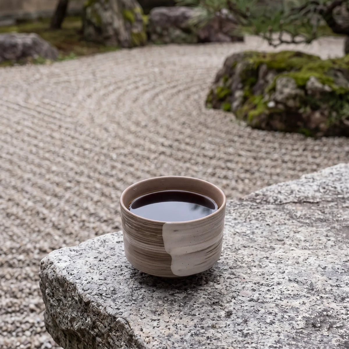 Swept Earth koffiekop op een granietblok bij een zandtuin